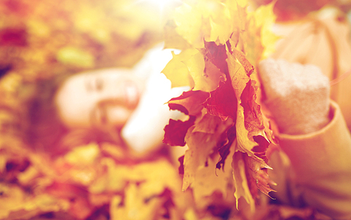 season and people concept - close up of beautiful young woman with autumn maple leaves lying on ground