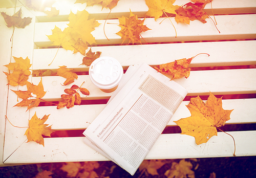 season and news concept - newspaper and coffee cup on bench in autumn park