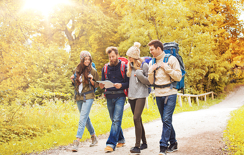 adventure, travel, tourism, hike and people concept - group of smiling friends walking with backpacks and map walking in autumn forest