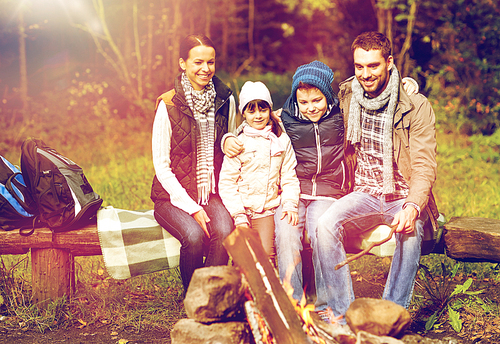 travel, tourism, hike and people concept - happy family sitting on bench at camp fire in woods
