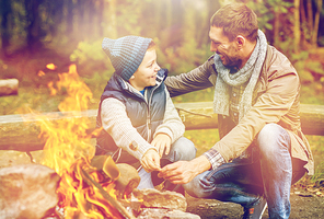camping, tourism, hike and family concept - happy father and son roasting marshmallow over campfire