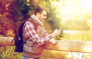 travel, tourism, hike and technology concept - happy man with backpack and smartphone outdoors