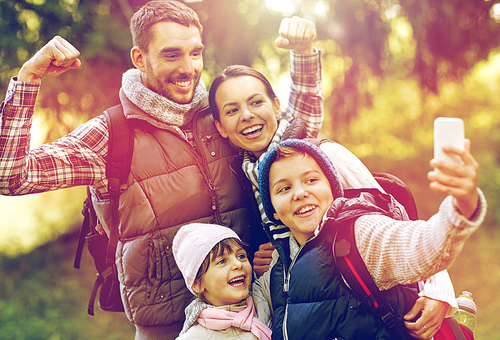 travel, tourism, hike and technology concept - happy family with backpacks taking selfie by smartphone outdoors