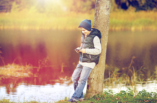 people, children and technology concept - happy teenage boy playing game or texting message on smartphone outdoors