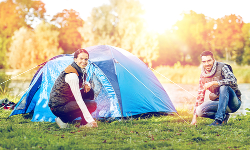 travel, tourism and hike concept - happy couple setting up tent outdoors