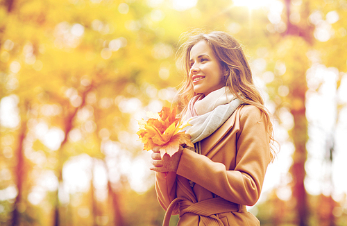 season and people concept - beautiful young woman with maple leaves walking in autumn park