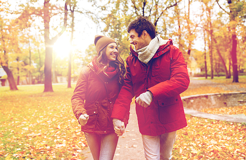 love, relationships, season and people concept - happy young couple walking in autumn park and talking