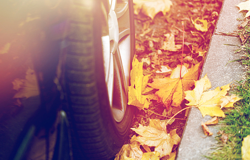 season and transport concept - close up of car wheel and autumn leaves