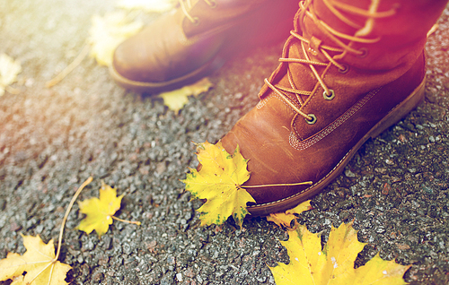 season, footwear and people concept - female feet in boots with autumn leaves on ground