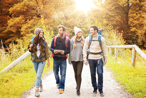 adventure, travel, tourism, hike and people concept - group of smiling friends with backpacks and tablet pc computer walking in autumn forest