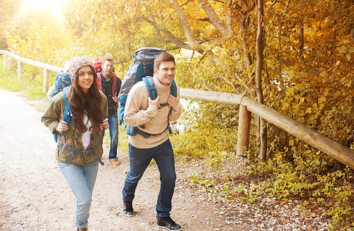 adventure, travel, tourism, hike and people concept - group of smiling friends walking with backpacks in autumn forest