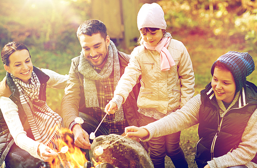 hike, travel, tourism and people concept - happy family roasting marshmallow over campfire