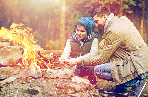 hike, travel, tourism and people concept - happy father and son roasting marshmallow over campfire