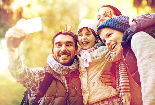 travel, tourism, hike and technology concept - happy family with backpacks taking selfie by smartphone outdoors