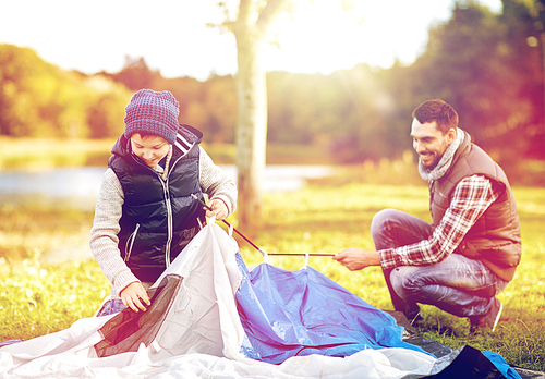 travel, tourism, hike and family concept - happy father and son setting up tent outdoors