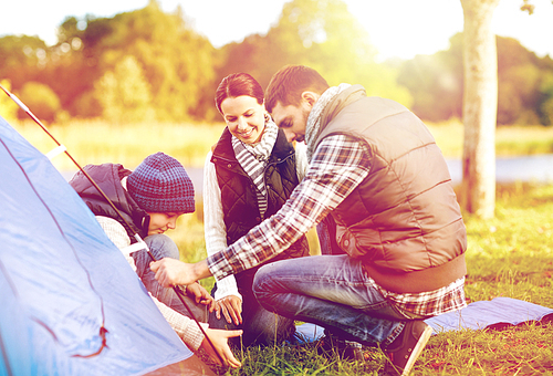 travel, tourism, hike and family concept - happy mother, father and son setting up tent outdoors