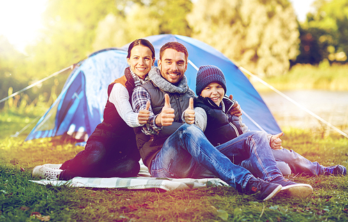 tourism, hike and travel concept - happy family over tent at camp site showing thumbs up gesture