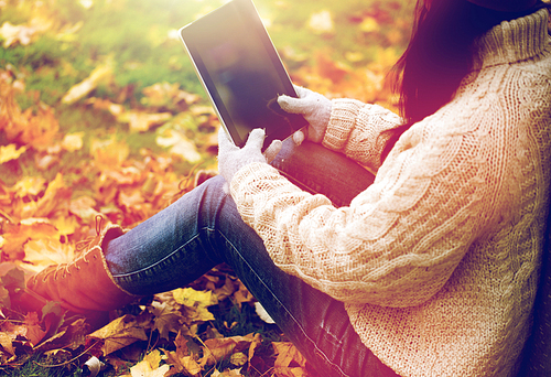 season, technology and people concept - close up of young woman with tablet pc computer sitting on grass in autumn park