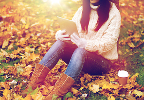 season, technology and people concept - young woman with tablet pc and coffee cup sitting on grass in autumn park