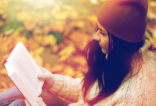 season, education, literature and people concept - close up of woman reading book in autumn park