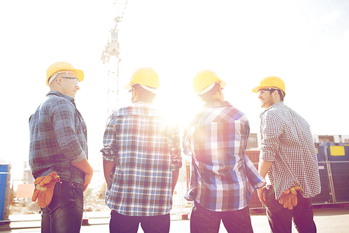 business, building, teamwork and people concept - group of smiling builders in hardhats outdoors from back