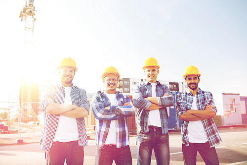 business, building, teamwork and people concept - group of smiling builders in hardhats with clipboard outdoors