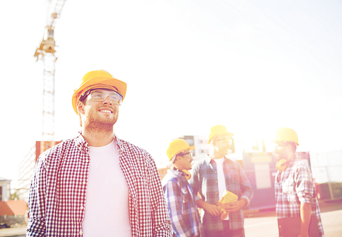 business, building, teamwork and people concept - group of smiling builders in hardhats with clipboard outdoors