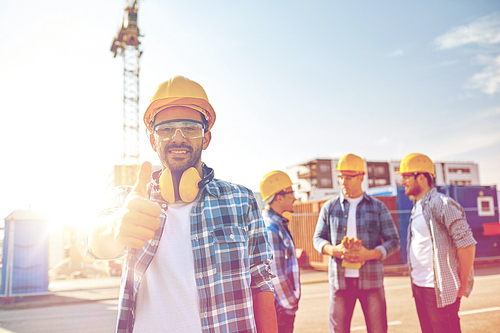 business, building, teamwork, gesture and people concept - group of smiling builders in hardhats showing thumbs up at construction site