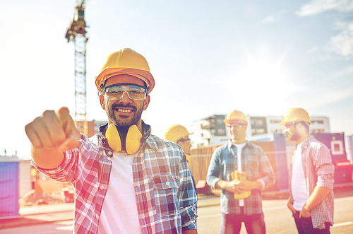 business, building, teamwork and people concept - group of smiling builders in hardhats pointing finger at you on construction site