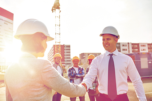 business, building, teamwork, gesture and people concept - group of smiling builders or architects in hardhats greeting each other by handshake on construction site