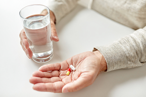 age, medicine, healthcare and people concept - close up of senior man hands with pills and water glass at home