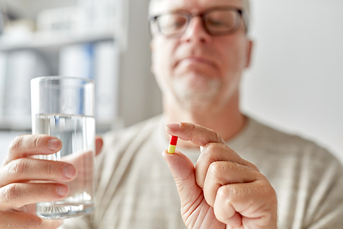 age, medicine, healthcare and people concept - close up of senior man hands with pill and water glass at home