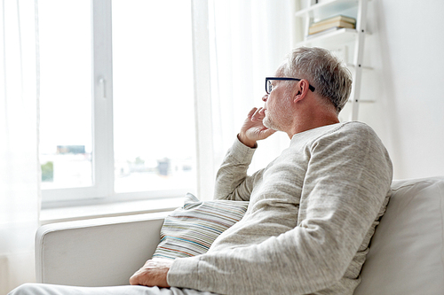 old age, problem and people concept - senior man in glasses thinking and looking through window at home