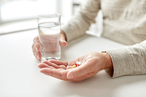 age, medicine, healthcare and people concept - close up of senior man hands with pills and water glass at home