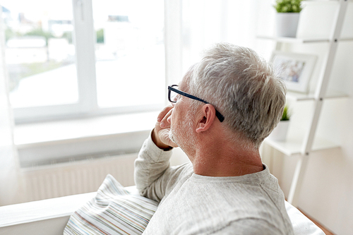 old age, problem and people concept - senior man in glasses thinking and looking through window at home