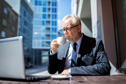 business, technology and people concept - senior businessman with laptop computer drinking coffee at city street cafe