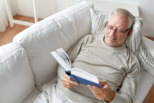 age, leisure and people concept - senior man lying on sofa and reading book at home