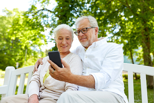 technology, relationship and old people concept - happy senior couple with smartphone taking selfie and hugging in summer