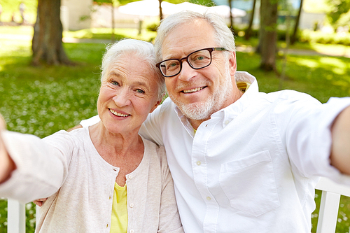 technology, relationship and old people concept - happy senior couple taking selfie and hugging at summer park