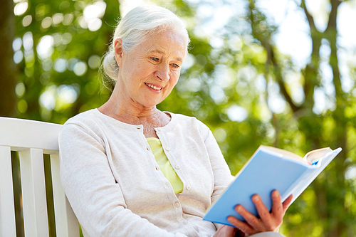 old age, retirement and people concept - happy senior woman reading book sitting on bench at summer park