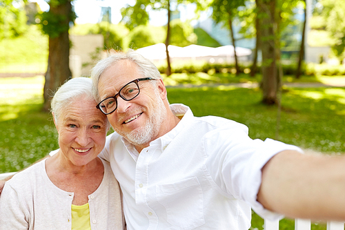 technology, relationship and old people concept - happy senior couple taking selfie and hugging at summer park