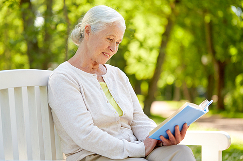 old age, retirement and people concept - happy senior woman reading book sitting on bench at summer park