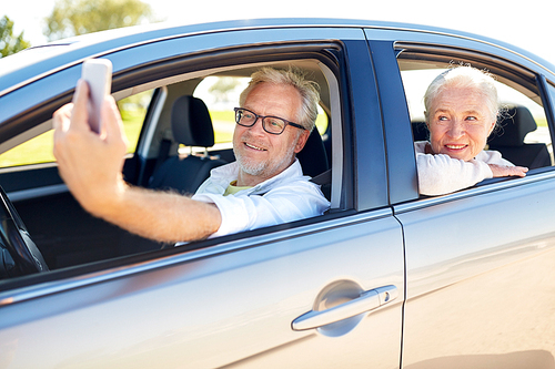 road trip, travel and old people concept - happy senior couple driving in car and taking selfie by smartphone