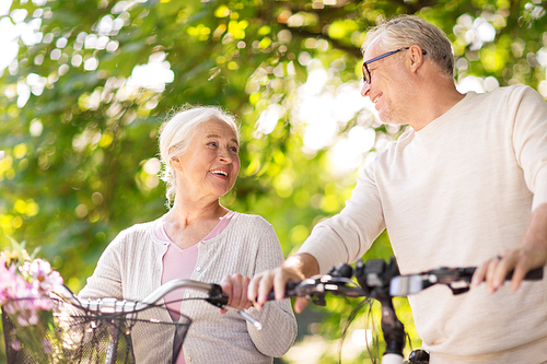 old age, people and lifestyle concept - happy senior couple walking with fixie bicycles talking at summer city park