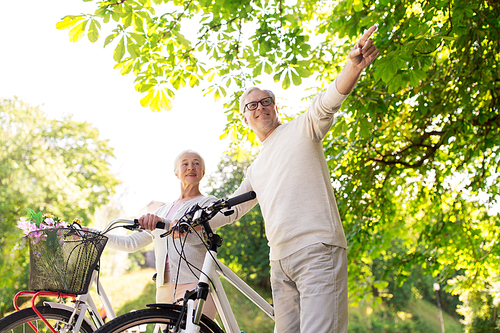 old age, people and lifestyle concept - happy senior couple walking with fixie bicycles at summer city park