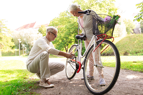 old age, people and lifestyle concept - happy senior couple with fixie bicycle at summer city park