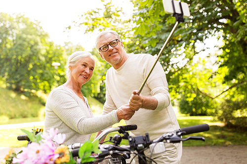 active old age, technology and lifestyle concept - happy senior couple walking with fixie bicycles taking selfie by smartphone at summer park