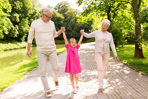 family, generation and people concept - happy smiling grandmother, grandfather and little granddaughter walking at park