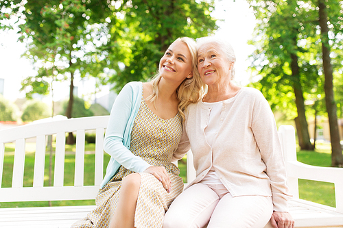 family, generation and people concept - happy smiling young daughter with senior mother sitting on park bench and hugging