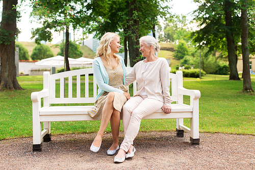 family, generation and people concept - happy smiling young daughter with senior mother sitting on park bench and hugging